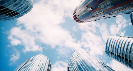 Round glass skyscrapers seen from below, against a blue sky with white clouds
